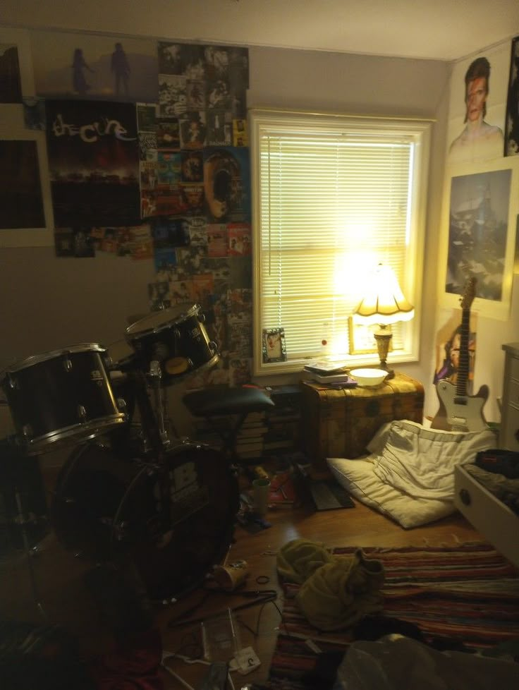 a bedroom with a drum set and various pictures on the wall behind it in front of a window