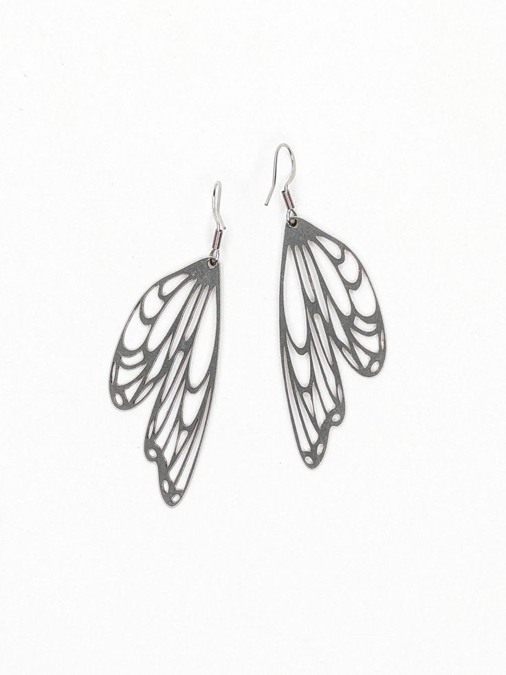 two pairs of silver earrings with wings on them, one in the shape of a butterfly