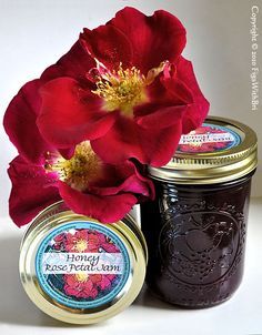 two jars filled with jam next to a red flower