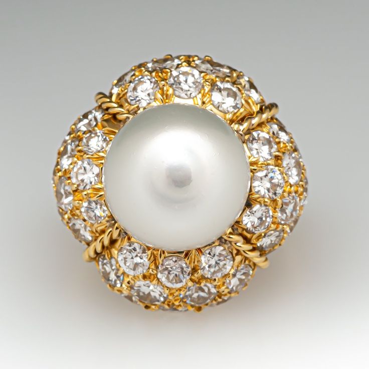 This magnificent cocktail ring is centered with one (1), post set, cultured South Sea pearl. The pearl tops a domed setting is bead set sixty-four (64), bead set, round brilliant cut diamonds. The ring has a split shank design and is accented with seven (7), bead set, round brilliant cut diamonds on each side. The ring measures 21.7mm at the top, rises 18.6mm above the finger, tapering to 2.4mm wide and 1.1mm thick at the base of the shank. The ring is currently size 7. Akoya Pearl Round Jewelry For Evening, Elegant White Domed Rings, Evening Akoya Pearl Jewelry, Round Diamond Pearl Ring, Elegant Domed Gemstone Jewelry, Elegant White Domed Jewelry, Classic Cabochon Pearl Ring For Formal Occasions, Luxury Pearl Cabochon Ring For Formal Occasions, Luxury Cabochon Pearl Ring For Wedding