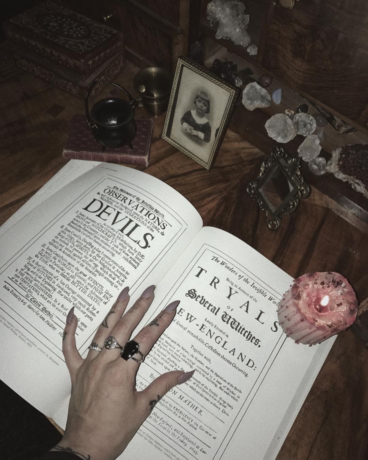 a person's hand on top of an open book next to flowers and candles