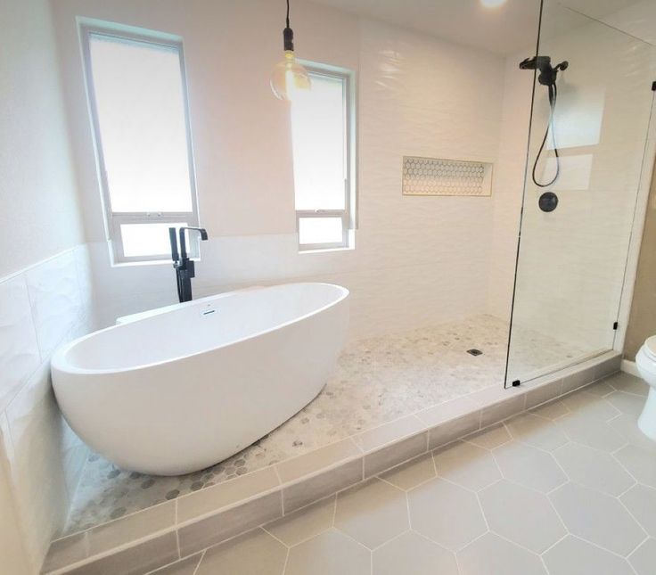 a large white bathtub sitting next to a toilet in a bathroom under two windows