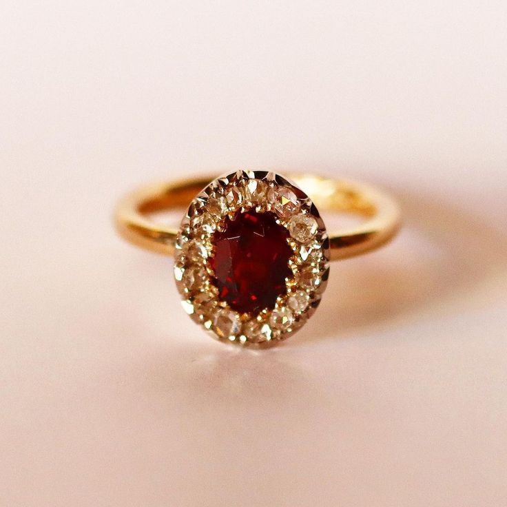 a gold ring with a red stone surrounded by small white and yellow diamonds on a pink surface