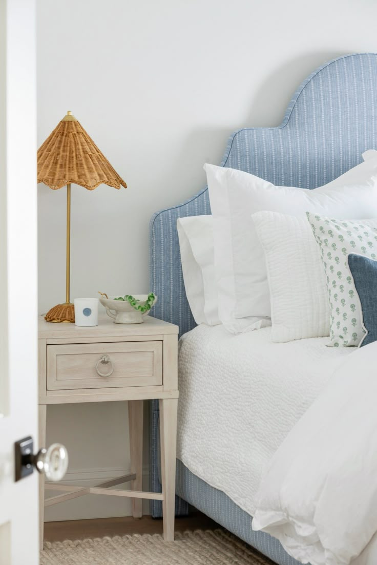 a bed with white sheets and blue headboard next to a lamp on a nightstand