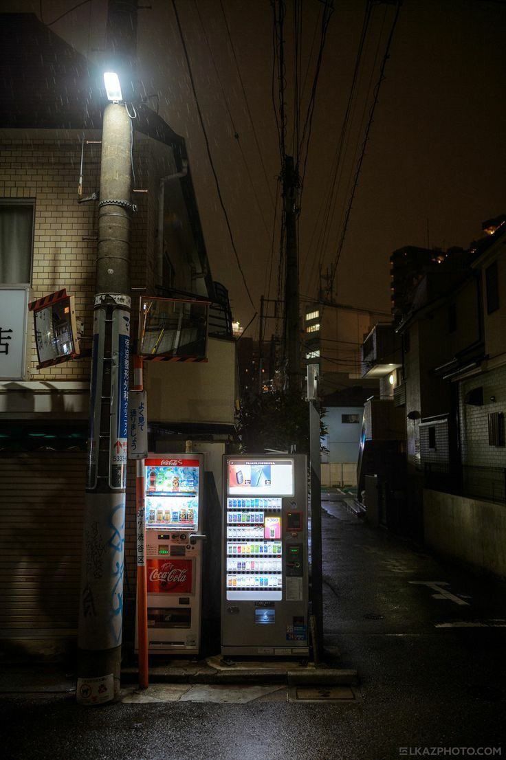 two vending machines sitting on the side of a road next to a building at night