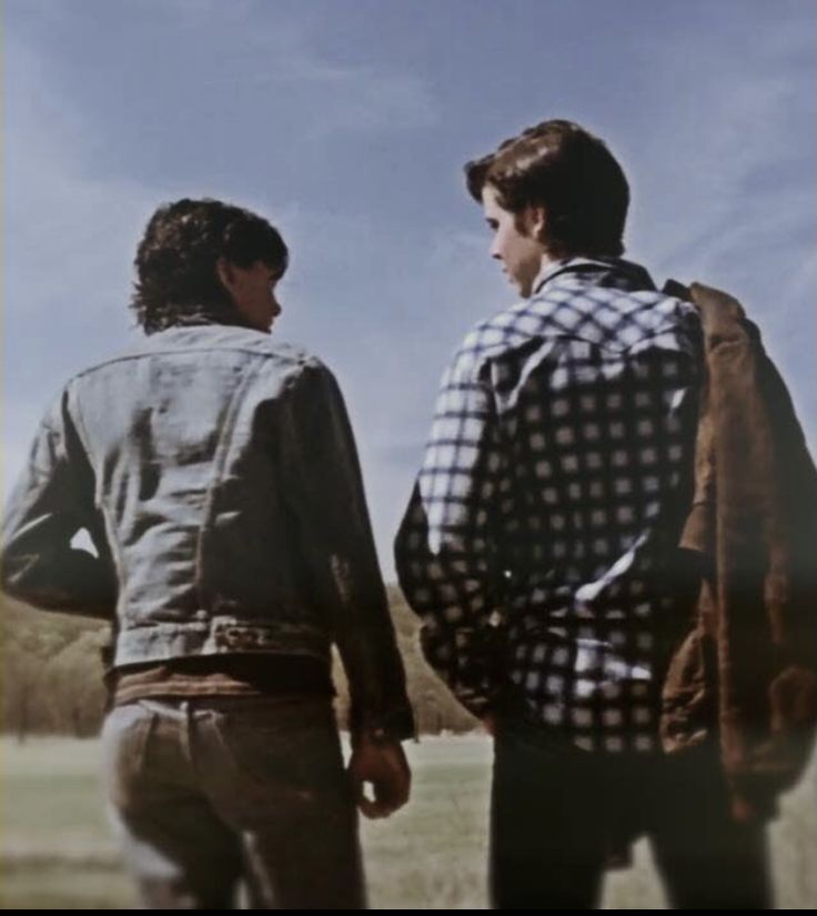 two men standing next to each other in front of a blue sky and grass field