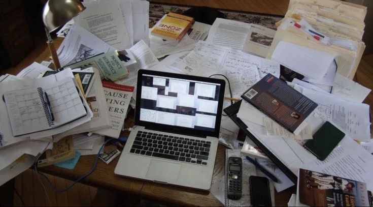 an open laptop computer sitting on top of a wooden desk covered in books and papers