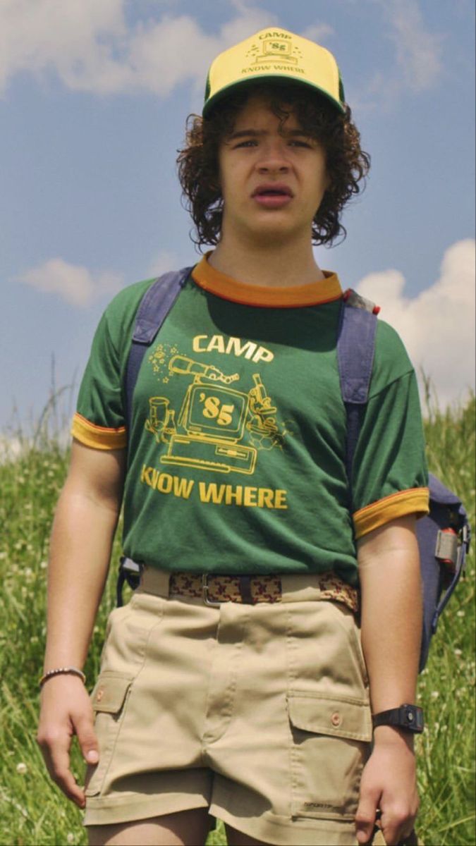 a young man standing in the grass wearing a hat and holding a frisbee