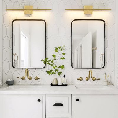 two mirrors on the wall in a bathroom with double sinks and gold faucets