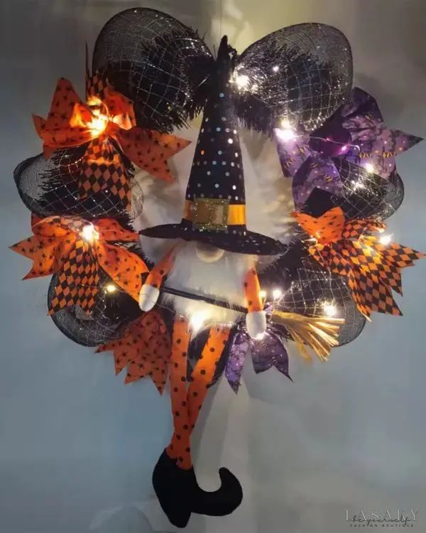 a halloween wreath made with mesh and lighted up pumpkins, witch's hat and broom