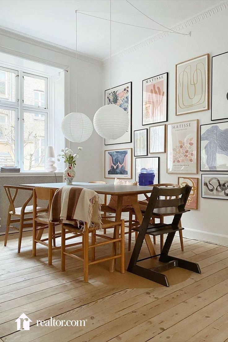 a dining room table with chairs and pictures on the wall in front of it's windows