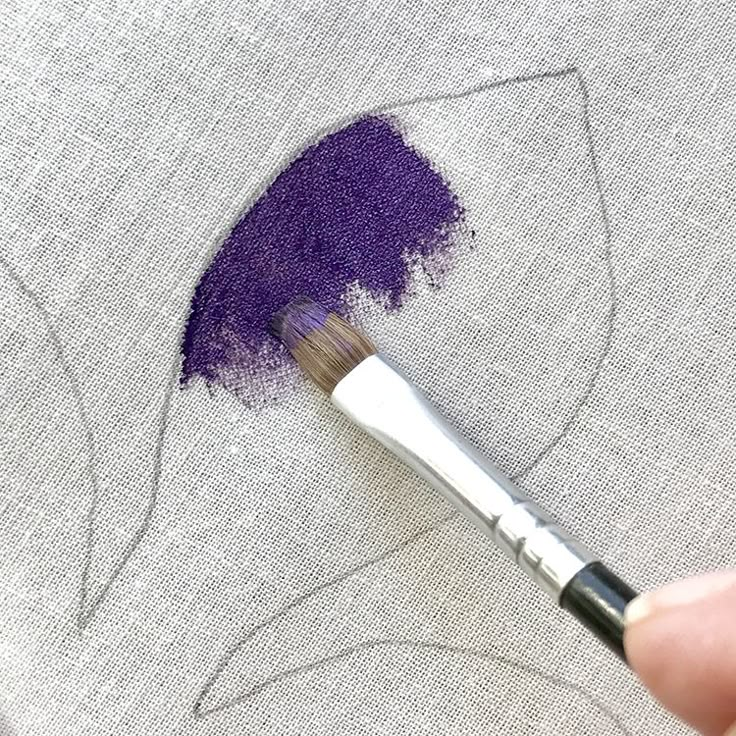 someone is using a brush to paint the design on a piece of fabric that has been stitched