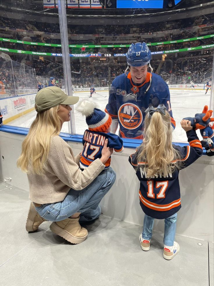 two women and a child are sitting on the ice with an edmonton oilers mascot in front of them