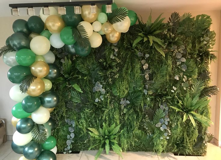 a green wall with balloons and greenery in the middle is decorated for an event