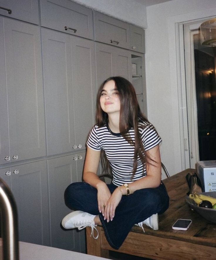 a woman sitting on top of a wooden table in a kitchen next to cupboards