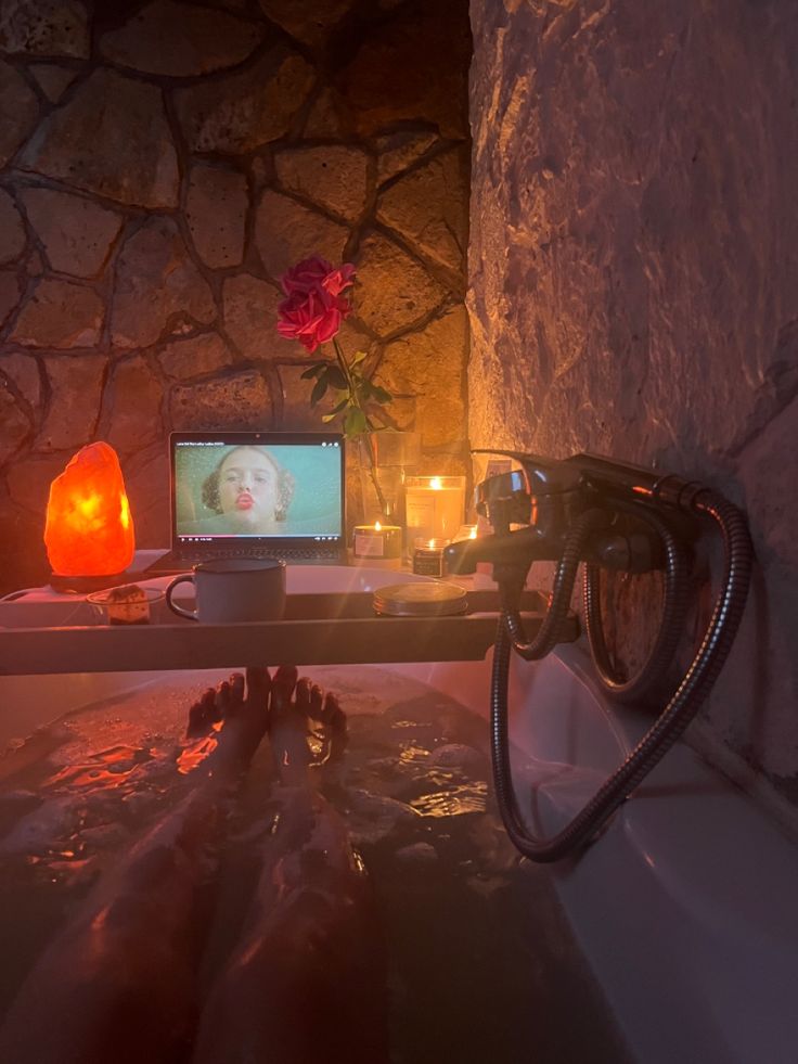 a person laying in a bath tub next to a laptop computer and candles on top of it