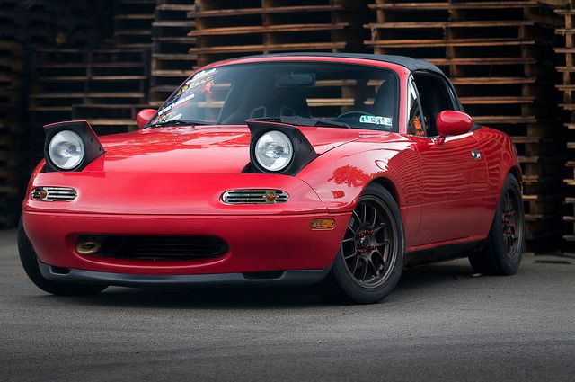 a red sports car parked in front of stacks of wood