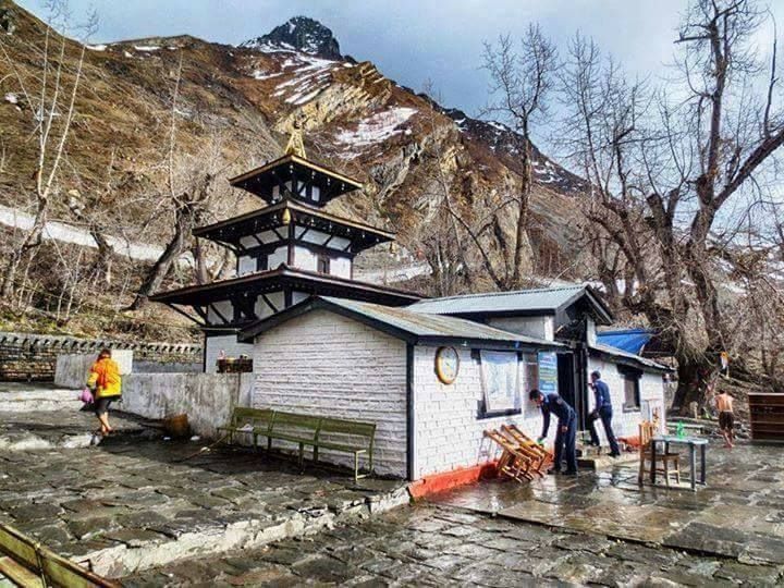 people are standing outside in front of a small building with a tower on top and mountains in the background