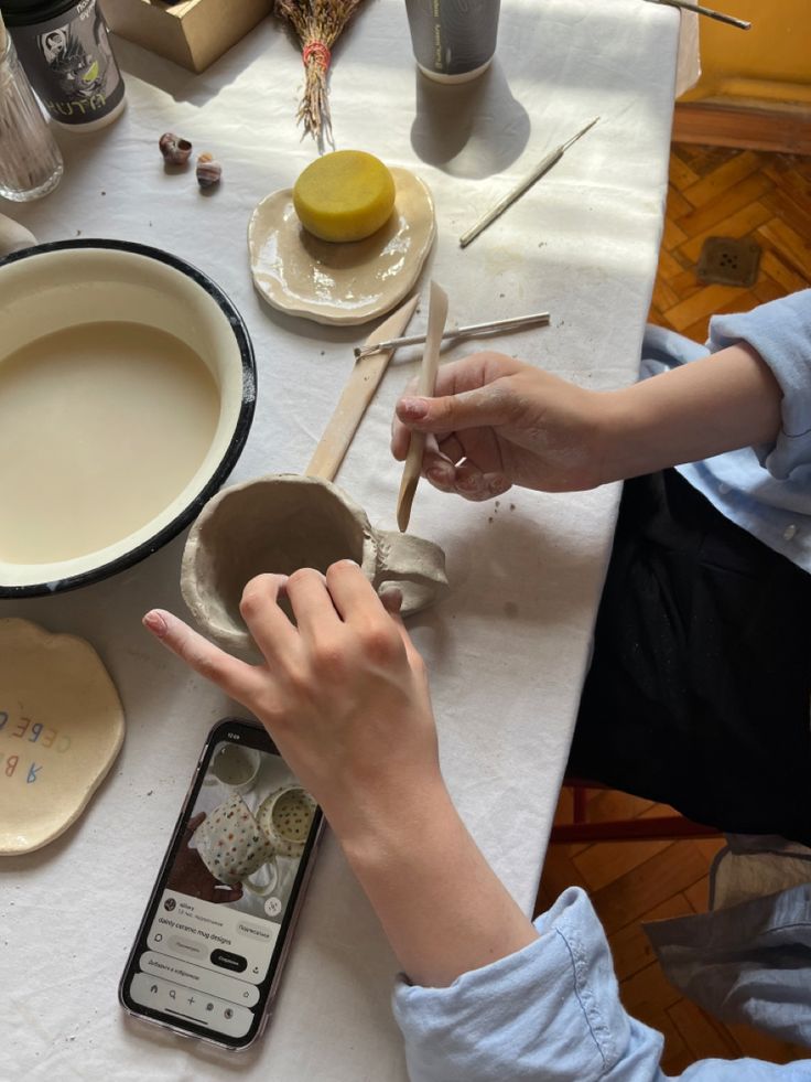 a person is making something out of clay on a table with other pottery and tools