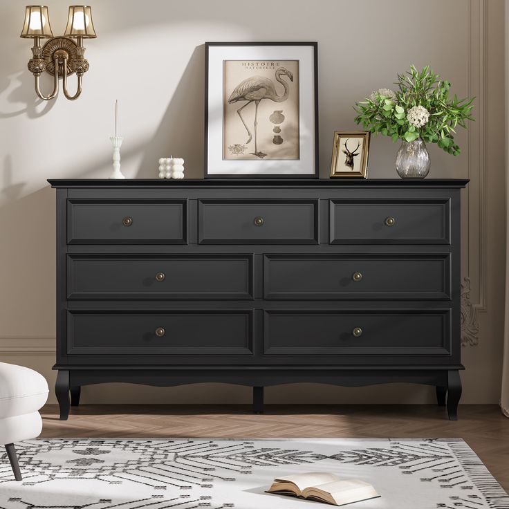 a black dresser with an open book and vases on it in a living room