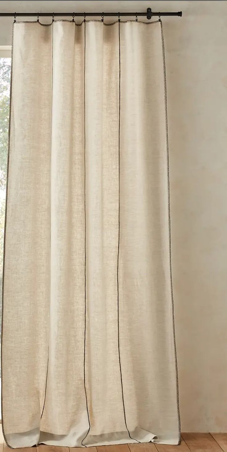 a white curtain hanging on the side of a window in front of a wooden floor