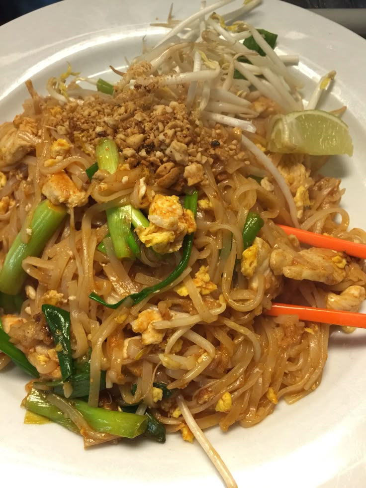 a white plate topped with noodles and veggies next to chopsticks on a table