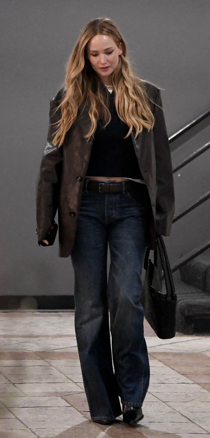 a woman walking down the street carrying a handbag in her right hand and wearing jeans on both sides