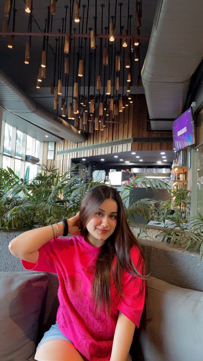 a woman sitting on top of a couch in front of a plant filled ceiling with hanging lights