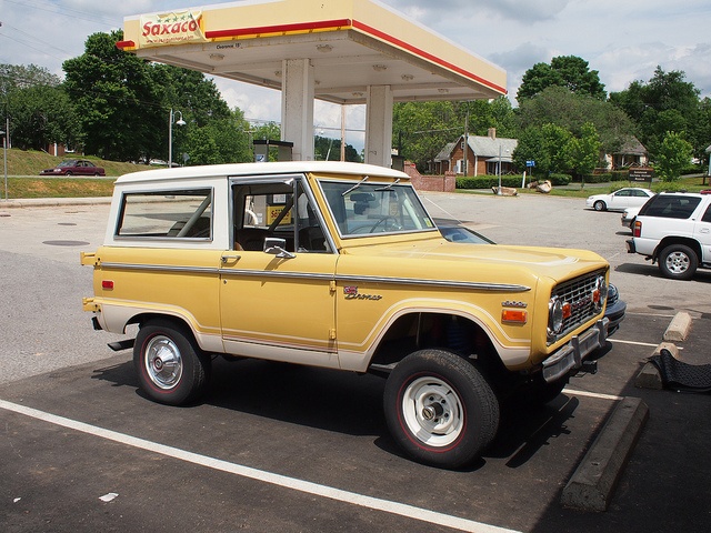 an old yellow truck parked in front of a gas station