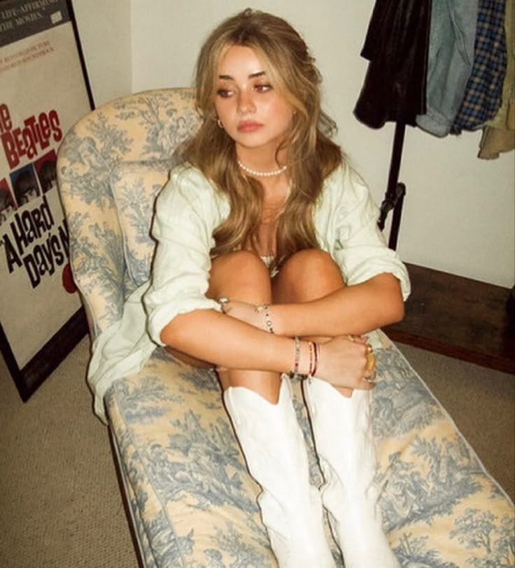 a woman sitting in a chair with her arms crossed and legs crossed, wearing white cowboy boots