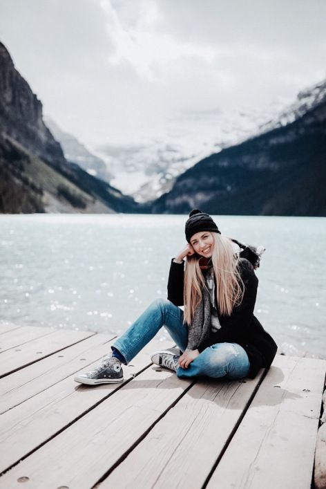 a woman is sitting on a dock by the water