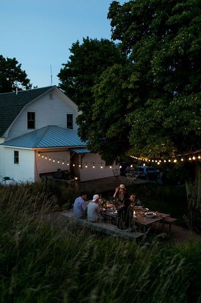 some people are sitting at a table outside by the house with string lights strung around it