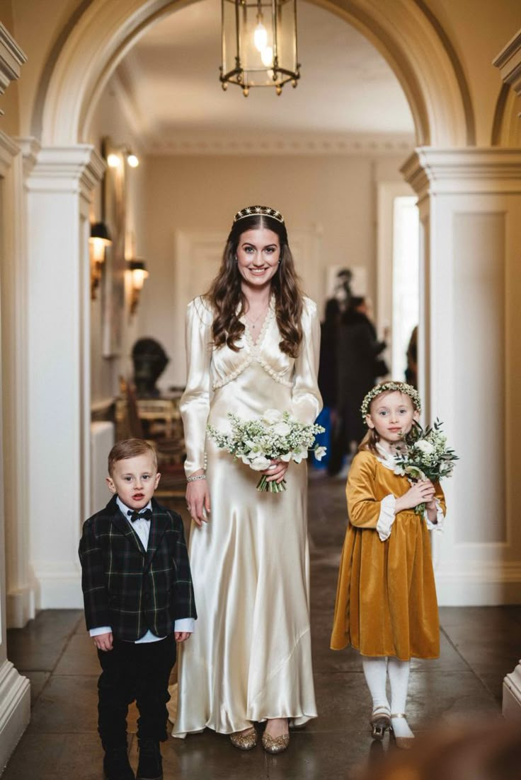 a woman in a white dress and two small children are walking down the hall together