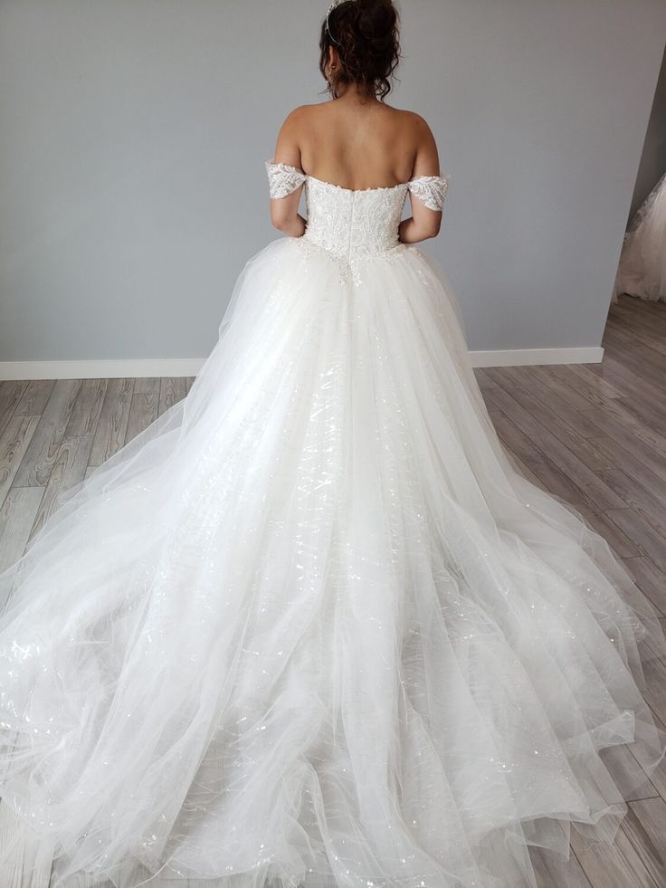 a woman in a white wedding dress standing on a wooden floor with her back to the camera