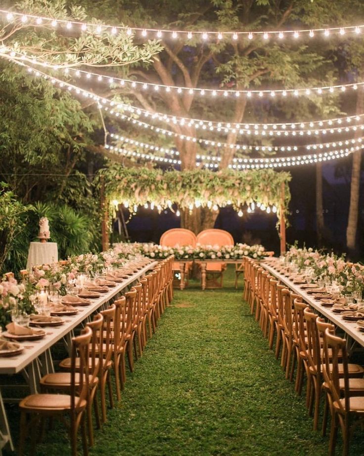 an outdoor wedding reception with string lights and wooden chairs, tables set up in the grass