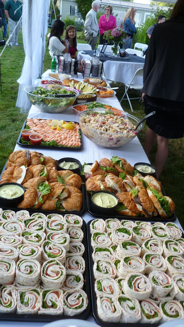 an assortment of sandwiches and rolls on a table at a wedding or other function with people in the background