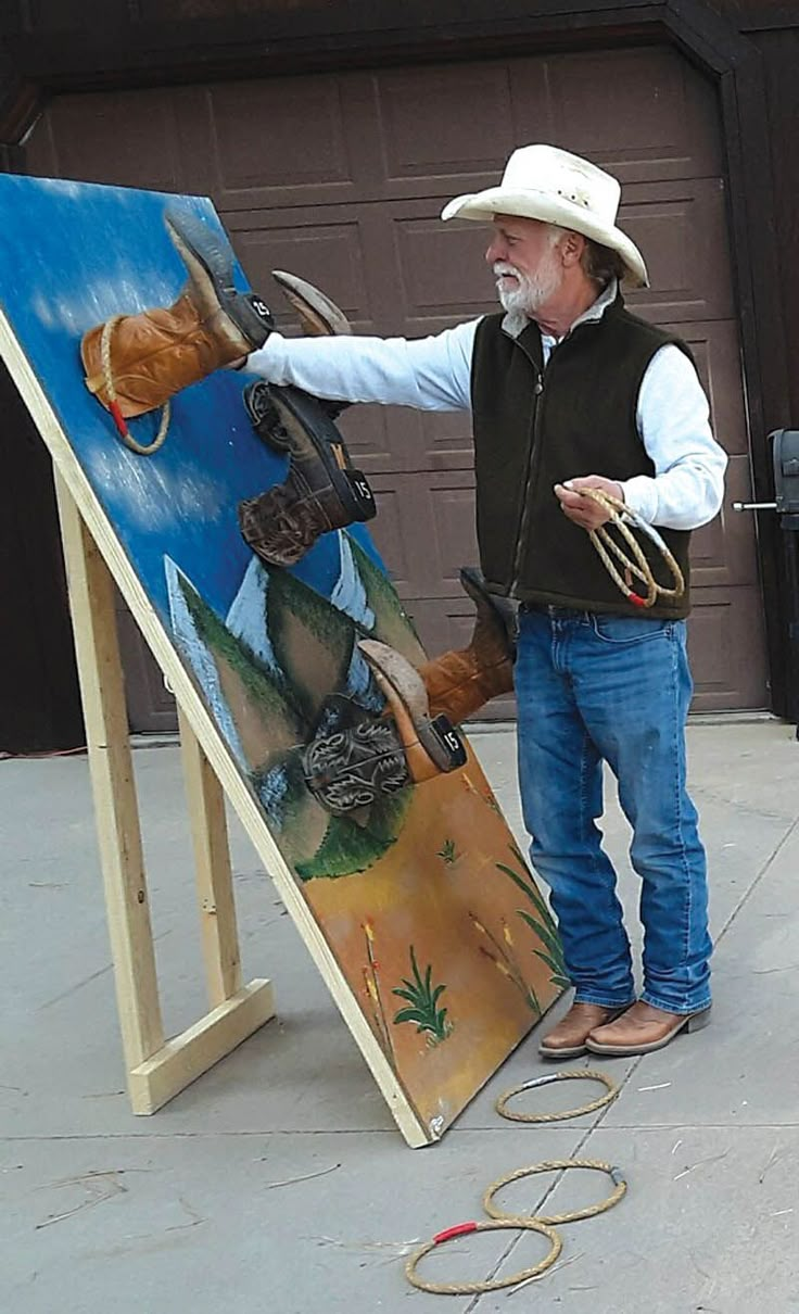 a man in cowboy hat standing next to an easel holding up a horse painting