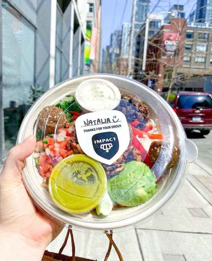 a person holding up a plastic container filled with different types of food on the street