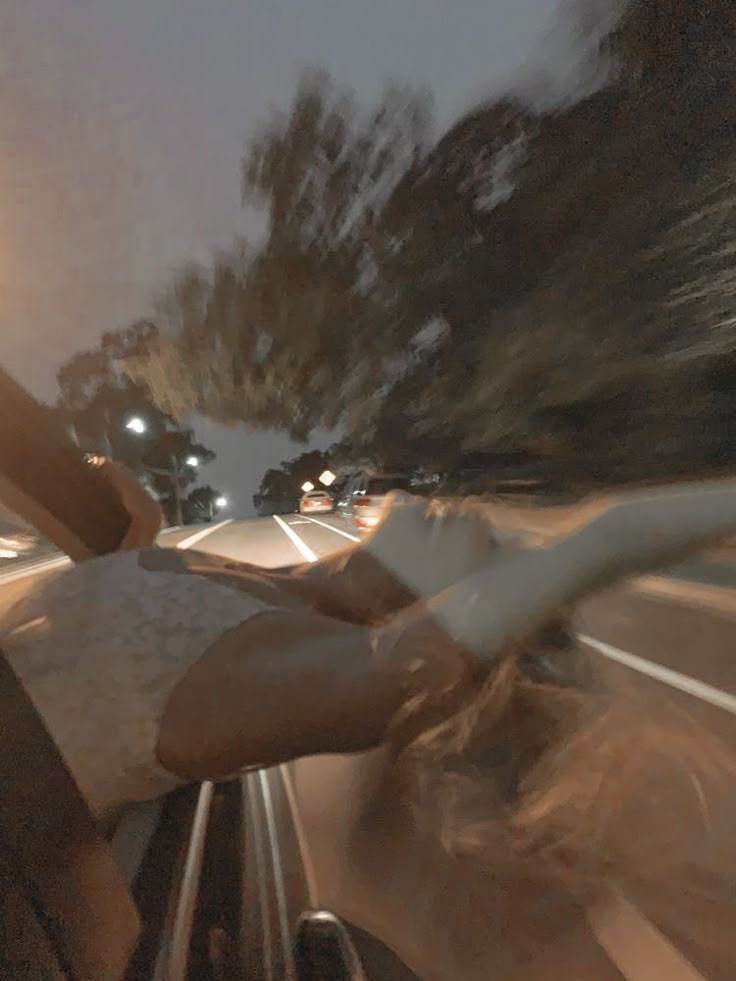 a person riding in a car on a street at night with their hand out the window