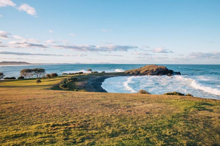 an ocean view from the top of a hill with waves crashing in to shore and green grass on both sides