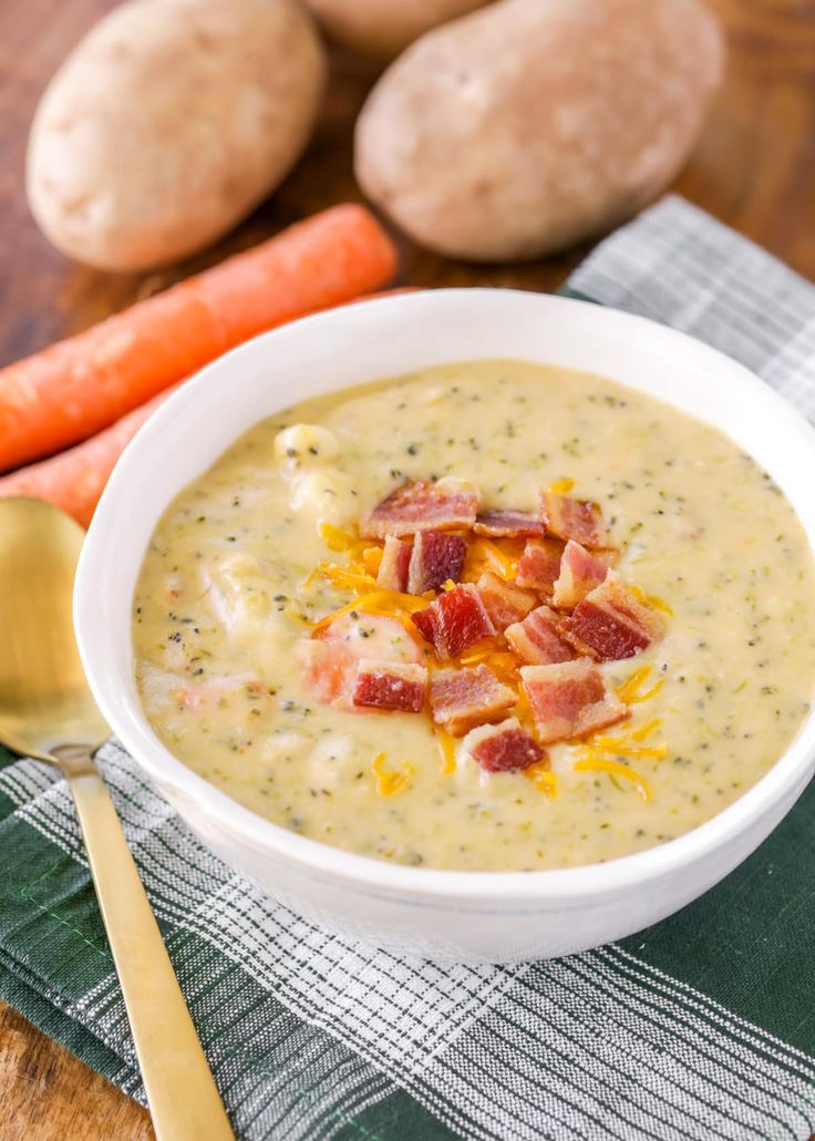 a bowl of soup with bacon and cheese in it next to carrots on a table