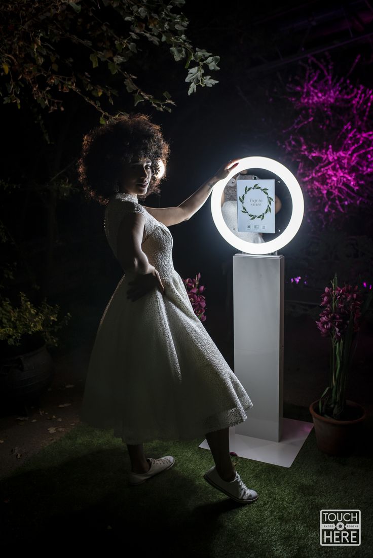 a woman in a white dress is standing next to a light up sculpture and holding her arm out