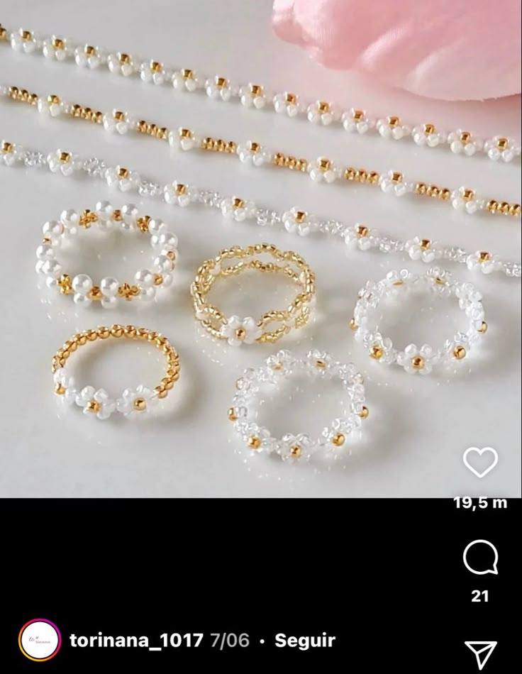 several different types of rings and bracelets on a white table next to a pink flower