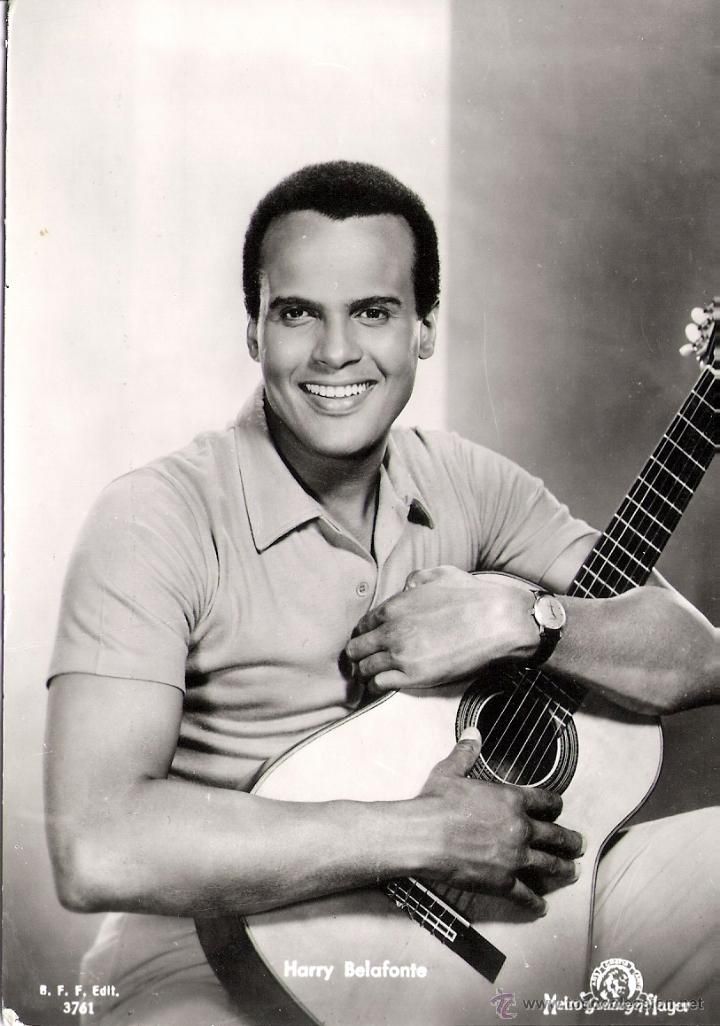 a black and white photo of a man holding an acoustic guitar in his right hand