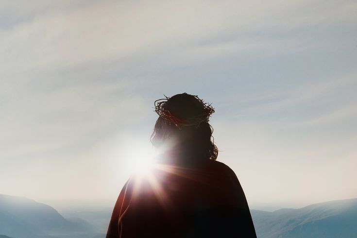 a person standing on top of a snow covered slope with the sun shining behind them