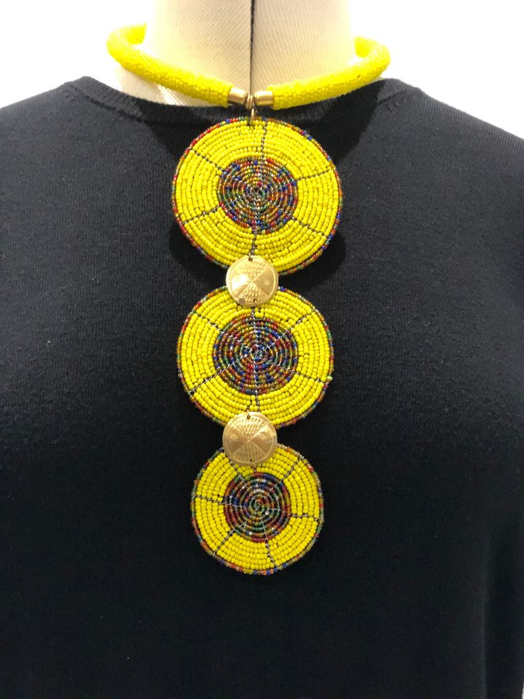 Africa wire beaded necklace, yellow beaded discs with multicoloured centres and multicoloured rim around the yellow disc.  2 gold discs join the 3 larger discs together. The 2 gold discs have an indented design on them.  There is a yellow beaded ring that the discs are attached to and fits around the neck.  The back of the necklace is closed by a hook clip.  We support local artisans in Zimbabwe and South Africa which is where this beautiful African Art Jewellery originates from.  Necklace lengt Multicolor Beaded Medallion Jewelry, Adjustable Yellow Necklaces With Polished Beads, Yellow Polished Beads Jewelry For Festival, Yellow Beaded Chain Necklace For Festivals, Adjustable Yellow Necklace With Polished Beads, Yellow Polished Round Beads Jewelry, Adjustable Round Beaded Necklace With Gold Beads, Yellow Round Beaded Necklaces For Festivals, Adjustable Yellow Necklace With Round Pendant