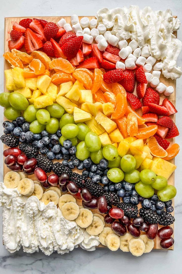 a rainbow made out of fruit and marshmallows on top of a cutting board