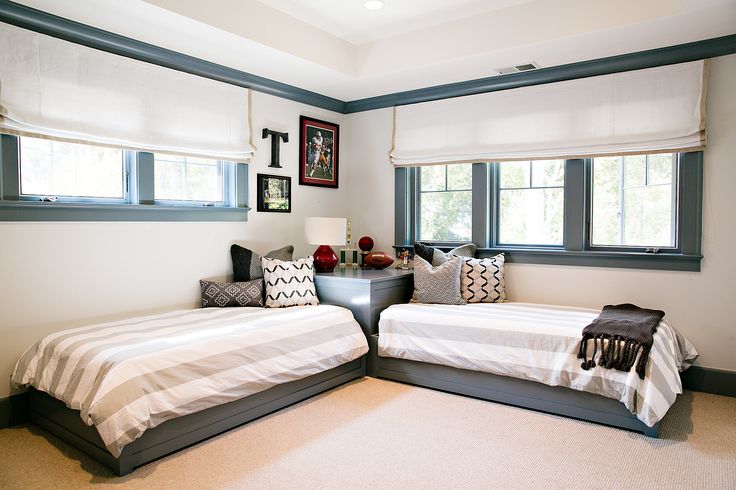 two twin beds in a bedroom with white walls and carpeted flooring next to windows