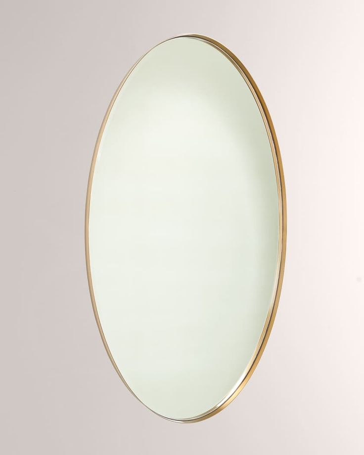 an oval mirror hanging on the wall in front of a white wall with gold trim