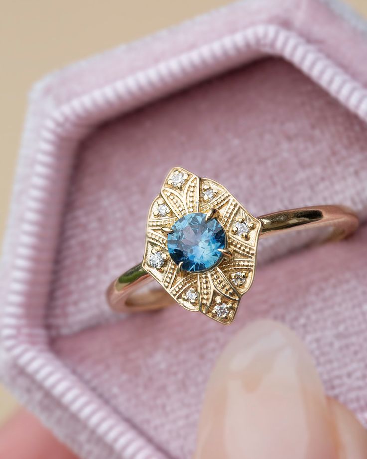 a close up of a person's hand holding a ring with a blue stone in it